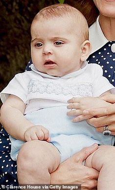 a woman holding a baby in her arms while wearing a polka dot shirt and earrings