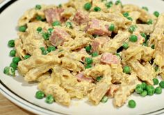 a white plate topped with pasta covered in meat and peas on top of a wooden table