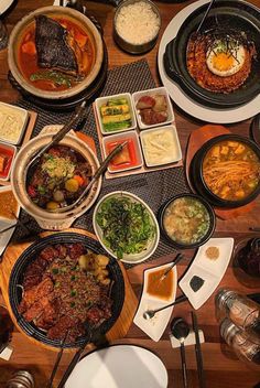 a wooden table topped with lots of different types of dishes and bowls filled with food