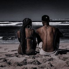 two people sitting on the beach looking out at the ocean