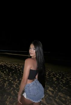 a woman standing on top of a beach next to the ocean with long black hair