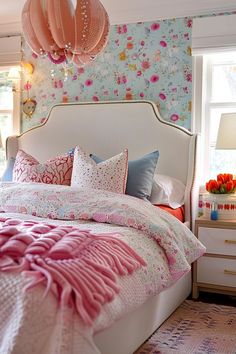 a bed with pink and blue pillows on top of it next to a window in a bedroom