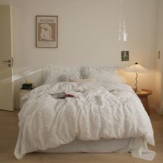 a bed with white comforter and pillows in a room next to a lamp on a table