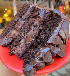 a piece of chocolate cake on a red plate with some chocolate chips around the edge