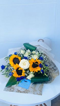 a bouquet of sunflowers and white roses on a table with blue ribbon around it