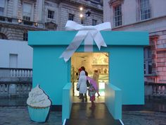 two people standing in front of a large blue box with a giant cupcake on it