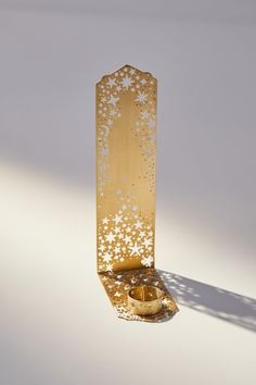 a gold candle holder with white stars on it and a shadow from the wall behind it