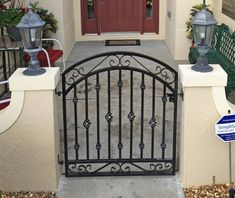 an iron gate in front of a house with potted plants on the side and a red door