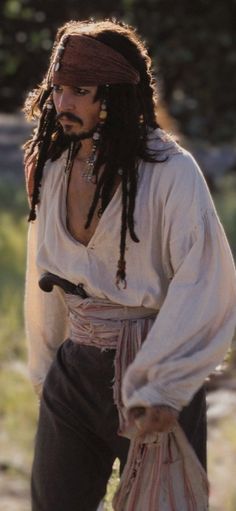 a man with dreadlocks is dressed in pirate clothing and carrying a bag on his shoulder