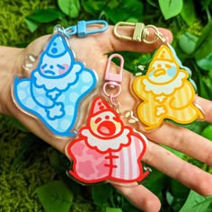 three different colored cartoon keychains on someone's hand with green leaves in the background