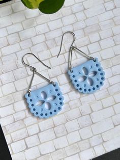 two pairs of blue earrings with holes in the middle on a white brick wall next to a potted plant