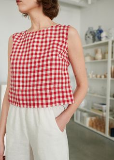 a woman wearing a red and white checkered top standing in front of a shelf