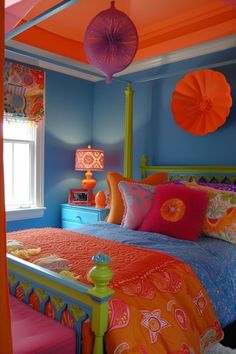 a bedroom with blue walls, orange and pink bedding and colorful decorations on the ceiling