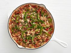 a pan filled with rice and vegetables on top of a white table next to a spoon