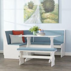 a white table with two benches and a blue bench cushion in front of a painting on the wall