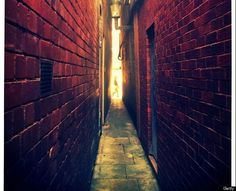 an alley way with red brick walls and light coming through the windows on either side