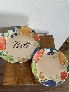 two colorful plates sitting on top of a wooden table with the word pasta painted on them