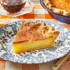 a piece of pie on a blue and white plate next to a cup of tea