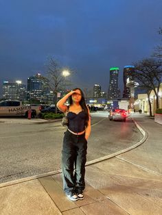 a woman standing on the side of a road in front of a cityscape