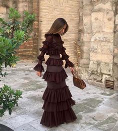 a woman in a long dress is walking down the street with her hand on her hip