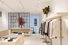 the inside of a clothing store with white walls and flooring, clothes on racks