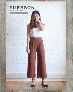 a woman standing in front of a white brick wall wearing wide legged pants and sandals