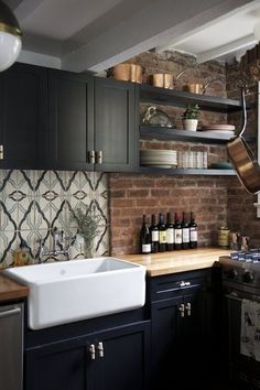 a kitchen with black cabinets, white sink and wooden counter tops in front of a brick wall