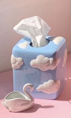 a tissue dispenser sitting on top of a pink table next to a white swan