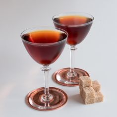 two wine glasses filled with red liquid next to some sugar cubes on a white surface