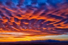 the sky is filled with colorful clouds as the sun sets over mountain range in the distance