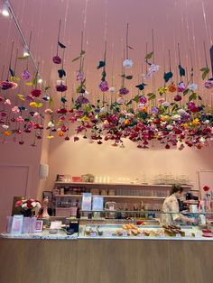 a woman standing in front of a counter with lots of flowers hanging from the ceiling