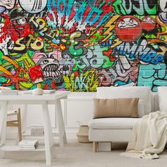 a living room with white furniture and colorful graffiti wallpaper on the brick wall behind it