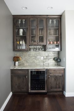 a kitchen with wooden cabinets and marble counter tops, wine glasses on the glass doors