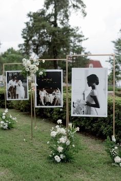 some pictures hanging on poles in the grass with flowers and greenery around them at a wedding