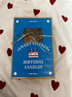 a blue birthday candle box with hearts on the bed and in the background is a sheet that says sweet sixteen