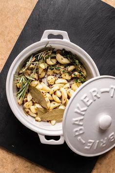 a casserole dish with potatoes and herbs in it, next to a lid