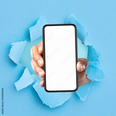 a person holding up a cell phone in front of a hole in the paper that has been torn open