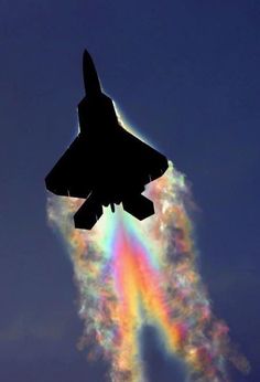 a jet flying in the sky with a rainbow behind it