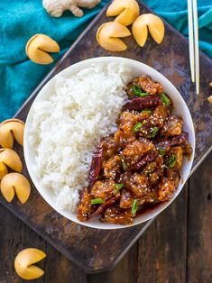 a white bowl filled with rice and meat on top of a wooden cutting board next to cashews