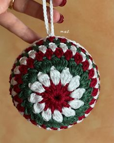 a crocheted christmas ornament hanging from a white string with red and green flowers