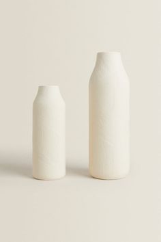 two white vases sitting next to each other on a gray surface, one is empty