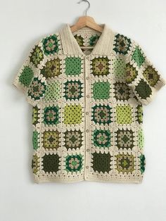 a green and white crocheted sweater hanging on a hanger