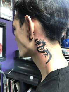 a man with a dragon tattoo on his neck and behind his ear, looking into the distance