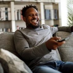 a man sitting on top of a couch holding a remote control in one hand and pointing to the other