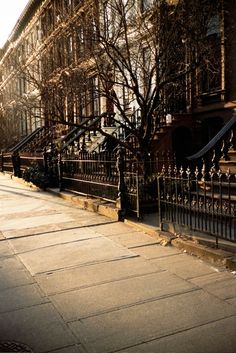 an empty sidewalk in front of a row of brownstone buildings with wrought iron railings