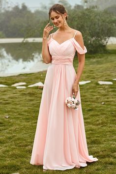 a woman in a long pink dress standing on the grass with her hand up to her face