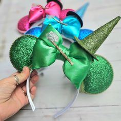 a hand holding a mouse ears with green, blue, and pink bows