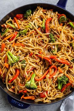 a skillet filled with noodles, broccoli and peppers on top of a table