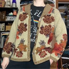 a woman standing in front of a bookshelf wearing a sweater with flowers on it