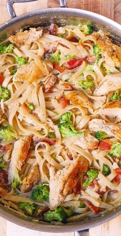 a skillet filled with chicken, pasta and broccoli on top of a wooden table